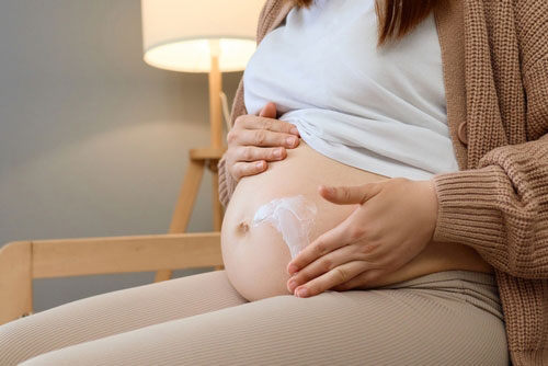 Donna incinta che applica una crema sulla pelle per alleviare i sintomi cutanei delle allergie.